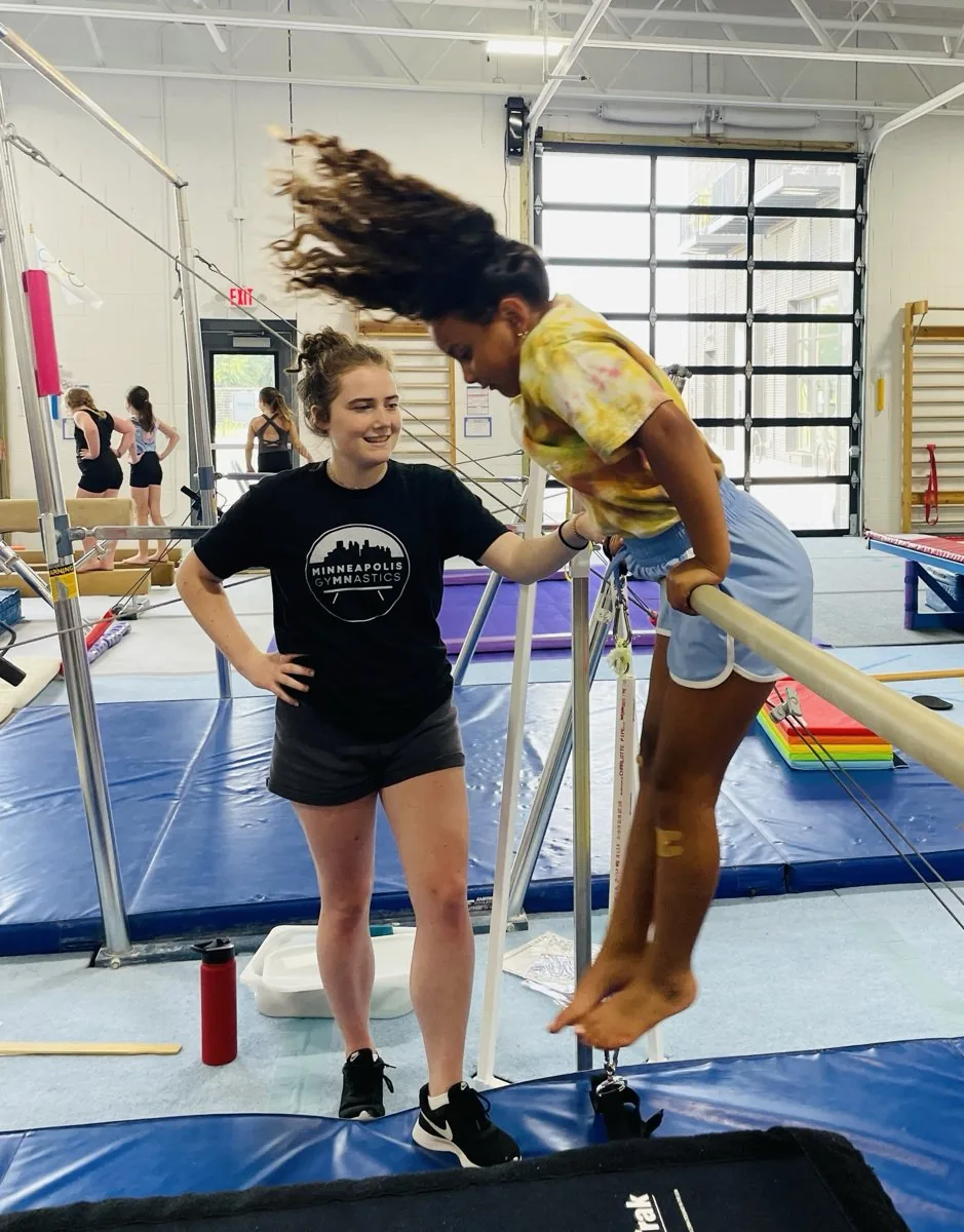 A coach spots a young gymnast swinging over the parallel bars