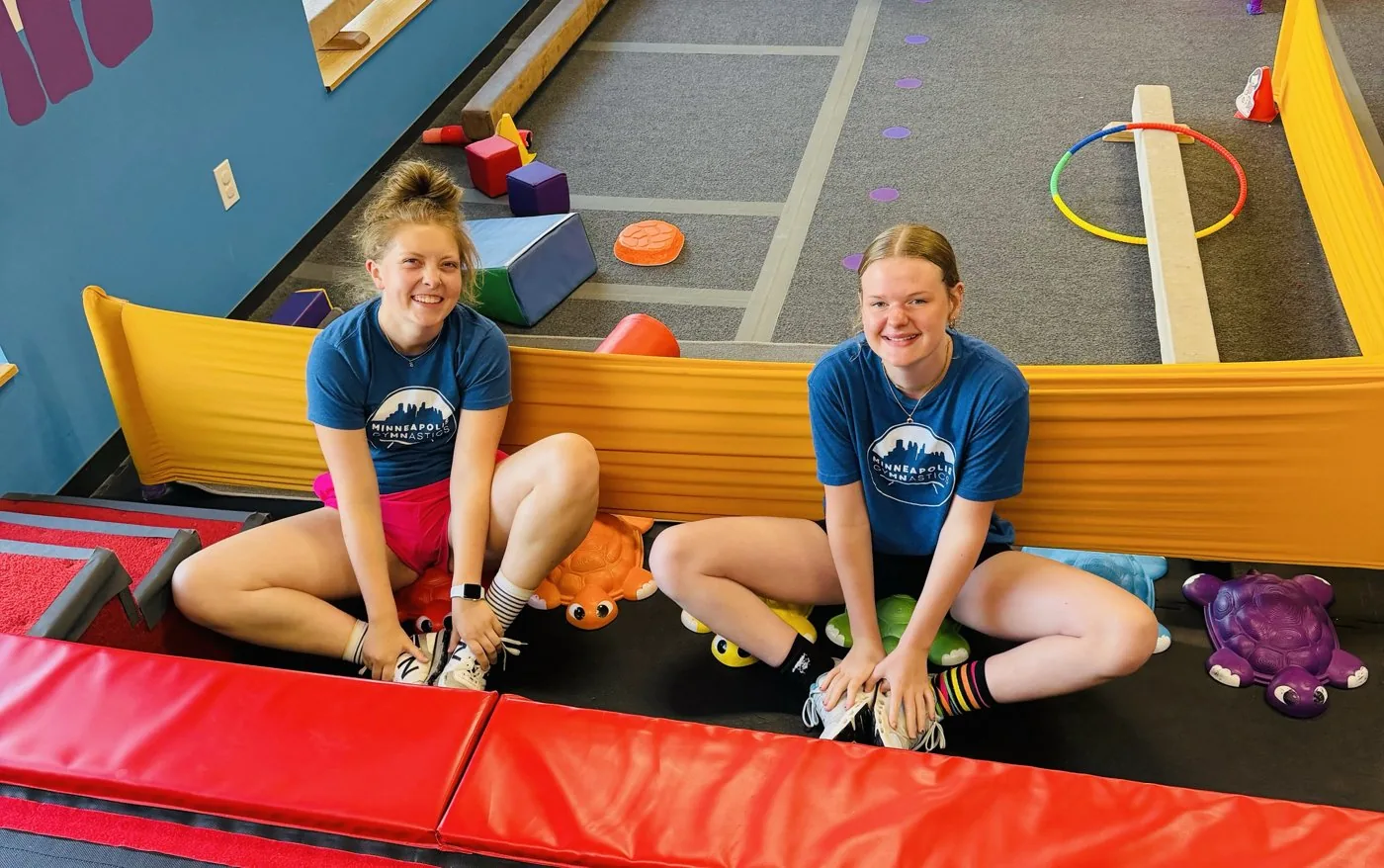 Two coaches sit together in the colorful preschool gym area