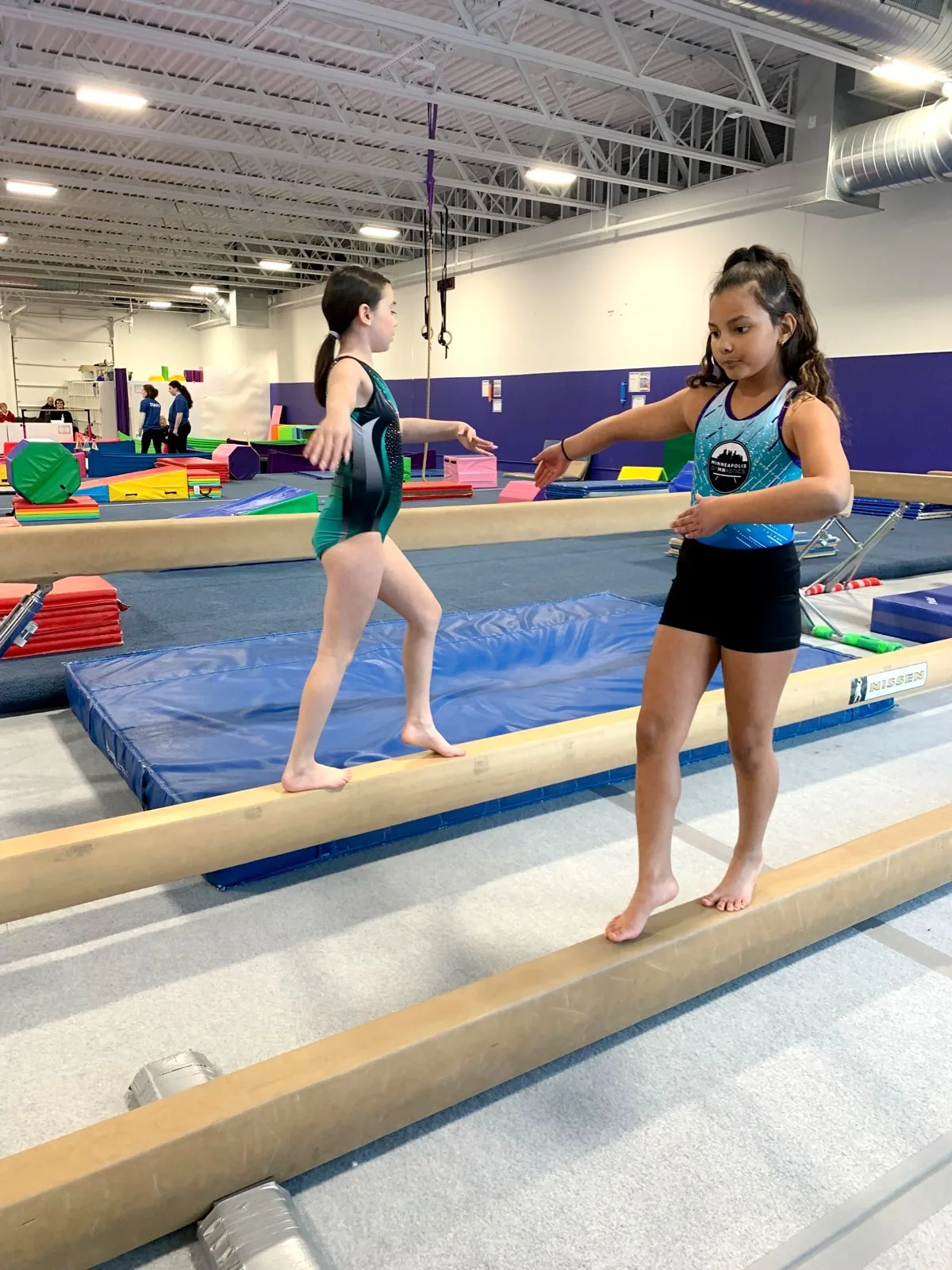 Two gymnasts practice balance side by side on low beams