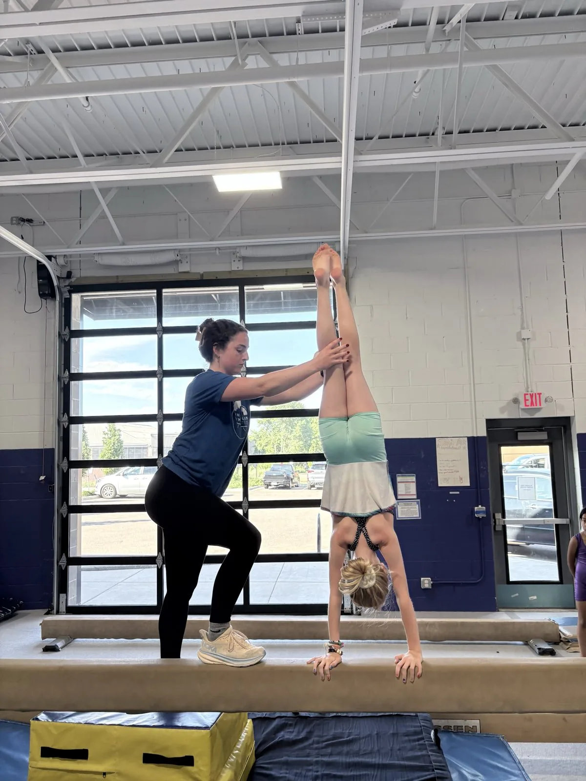 A coach spots a gymnast holding a handstand on the beam